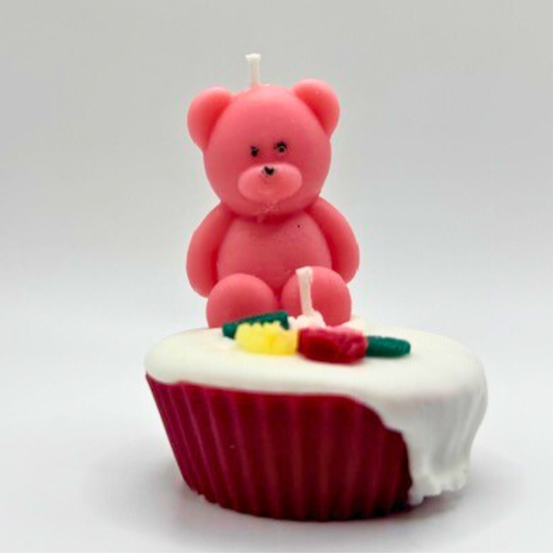 A double wicks cupcake candle in pink, decorated with a teddy bear and flowers on top.