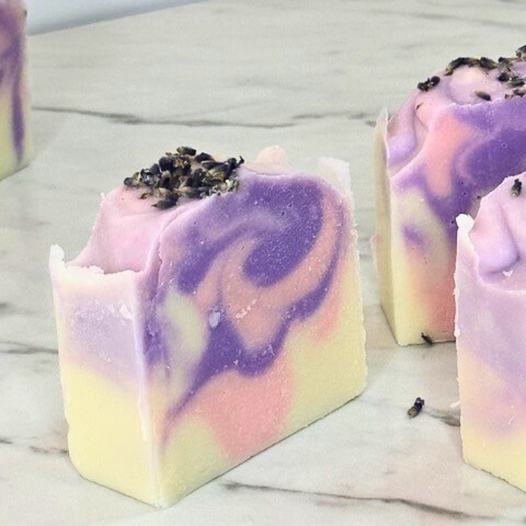 A white soap bar with a pink and purple swirl in the center, topped with natural lavender buds.