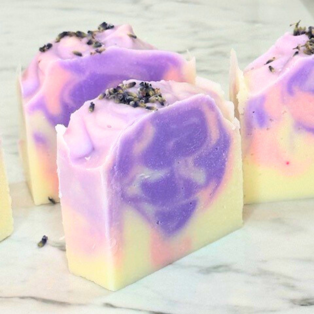 A white soap bar with a pink and purple swirl in the center, topped with natural lavender buds.