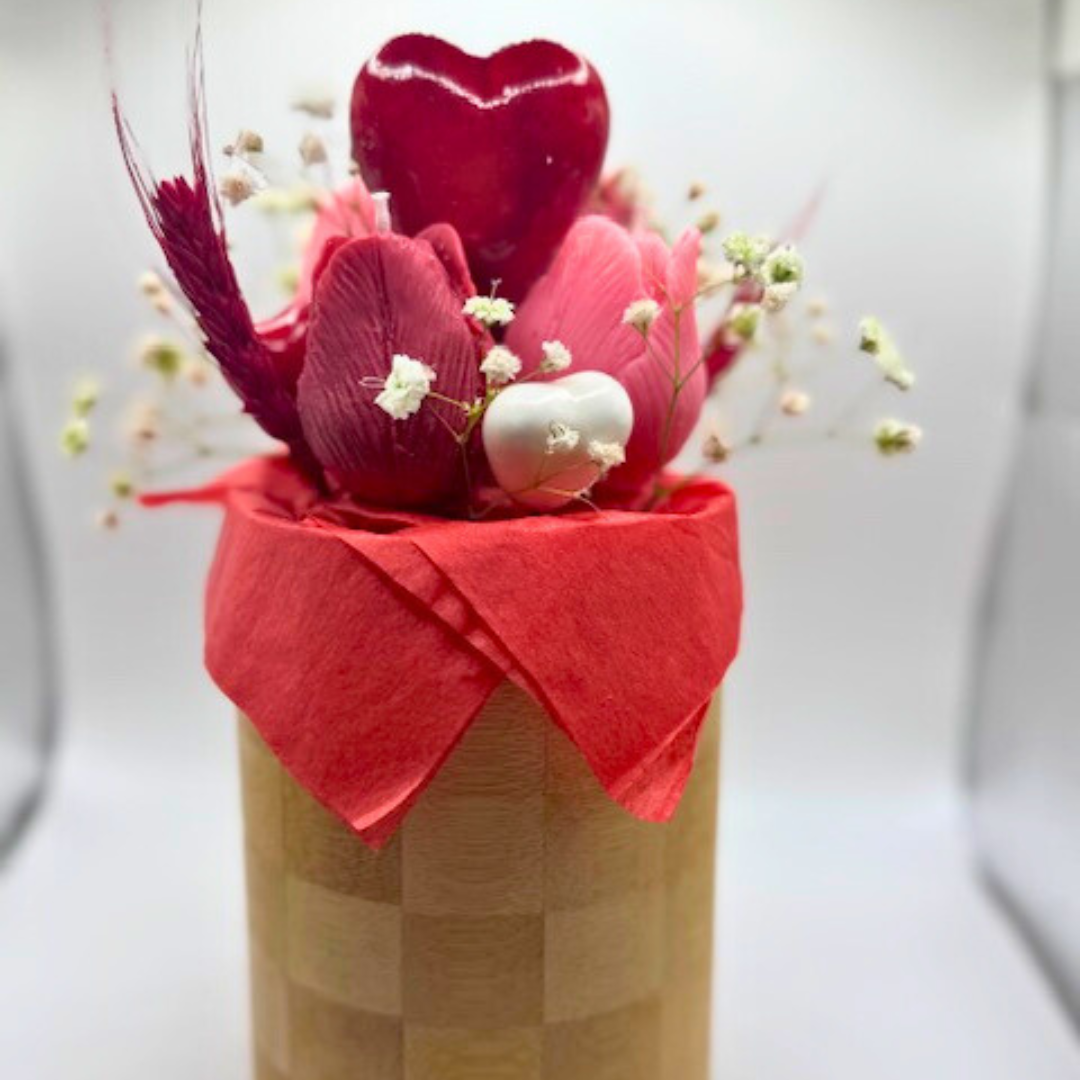A wooden vase filled with candles shaped like pink and red roses. decorated with big red heart in the middle and botanical flora with many other small hearts