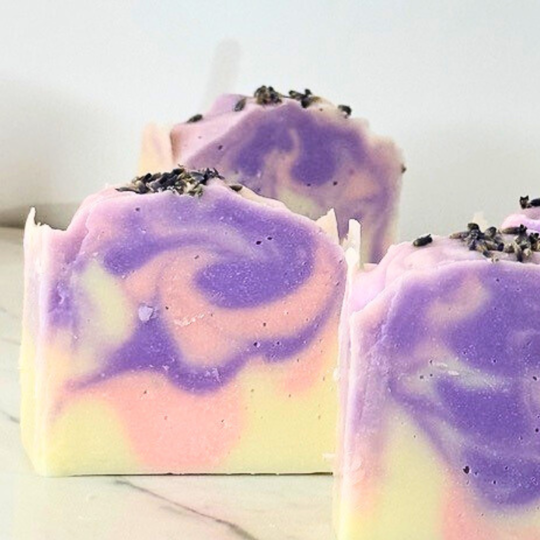 A white soap bar with a pink and purple swirl in the center, topped with natural lavender buds.