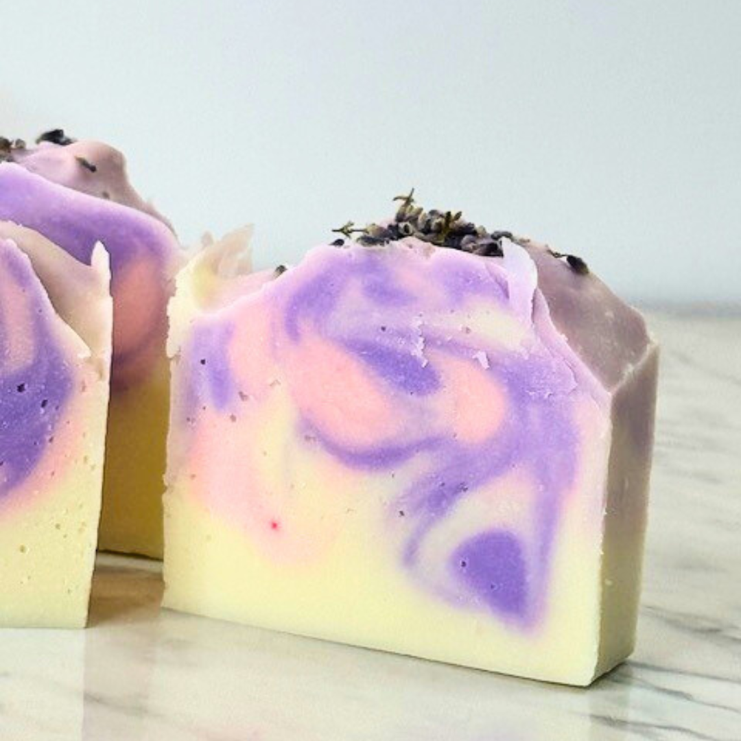 A white soap bar with a pink and purple swirl in the center, topped with natural lavender buds.