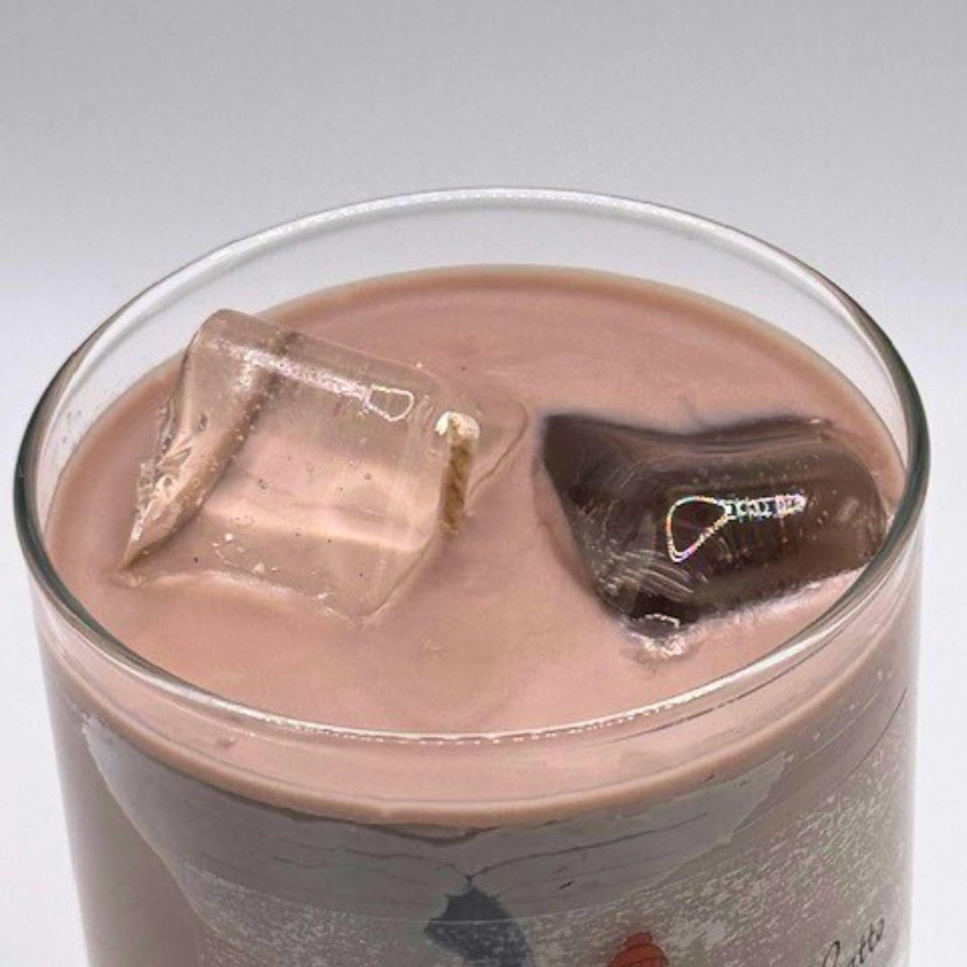 A single-wick candle in a clear jar, designed to resemble an iced latte, with a white layer at the bottom, a rich brown coffee-colored wax, and a clear ice cube detail on top.