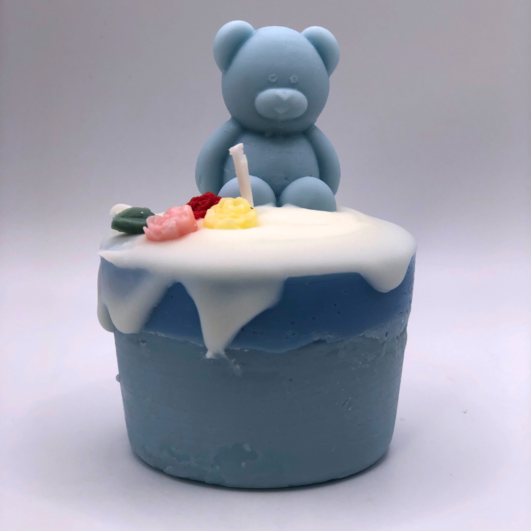 A single wick cupcake candle in baby blue, decorated with a teddy bear and flowers on top.