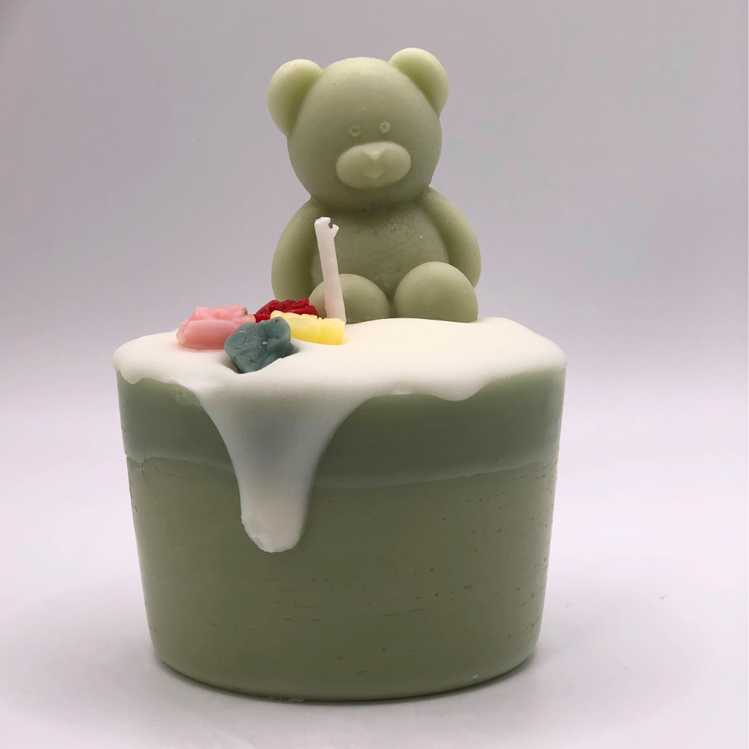 A single wick cupcake candle in light green, decorated with a teddy bear and flowers on top.