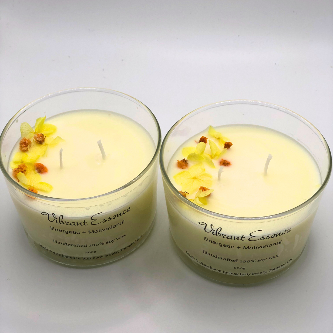 A single-wick white candle in a clear jar, topped with a dried yellow and orange floral decoration.