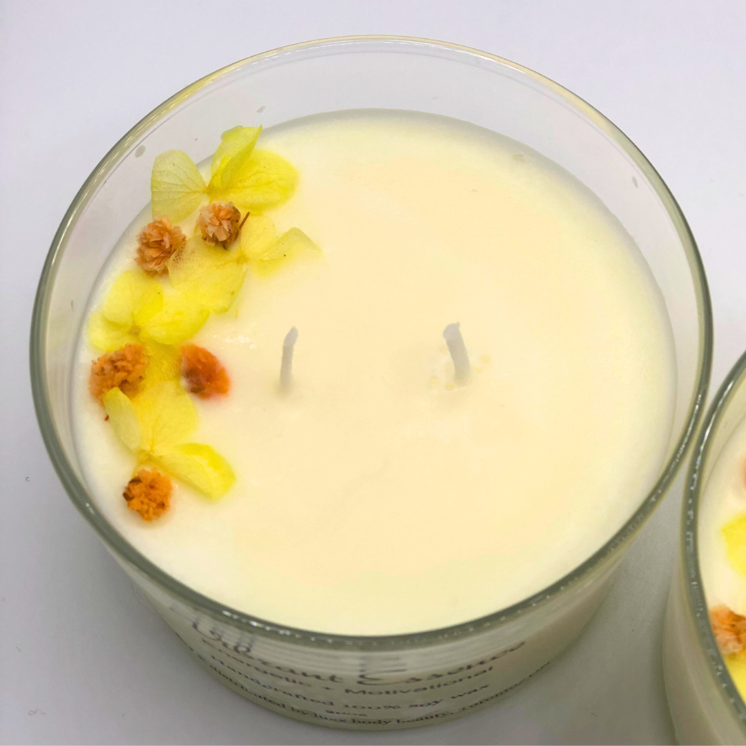 A single-wick white candle in a clear jar, topped with a dried yellow and orange floral decoration.