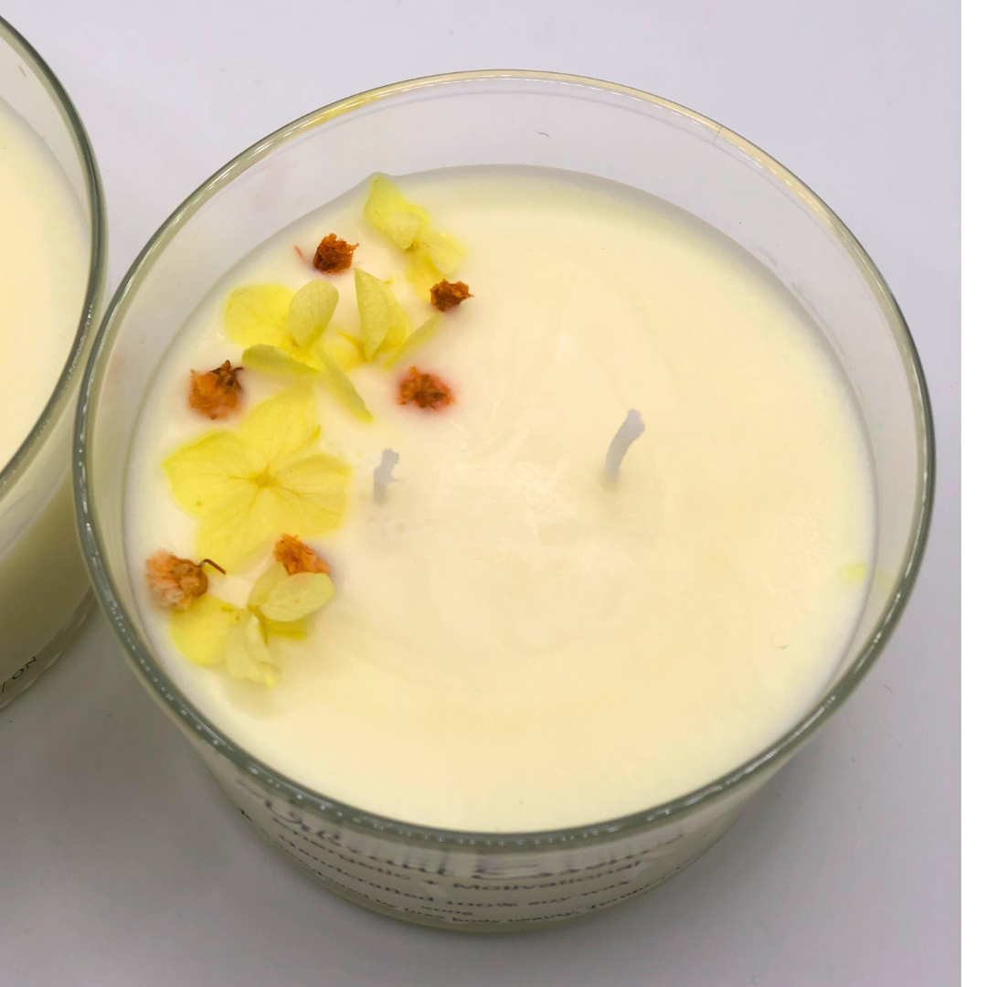 A single-wick white candle in a clear jar, topped with a dried yellow and orange floral decoration.