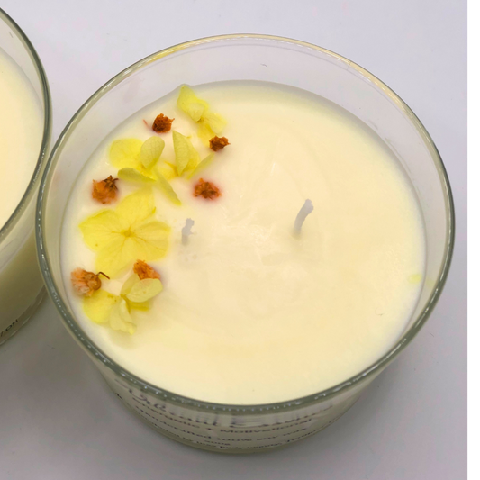 A single-wick white candle in a clear jar, topped with a dried yellow and orange floral decoration.