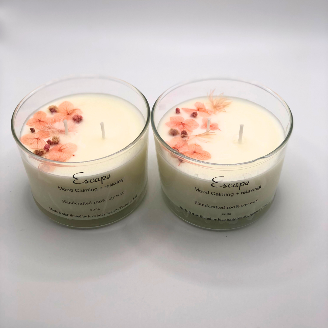 A single-wick white candle in a clear jar, topped with a dried pink floral decoration.