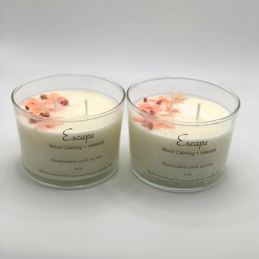 A single-wick white candle in a clear jar, topped with a dried pink floral decoration.