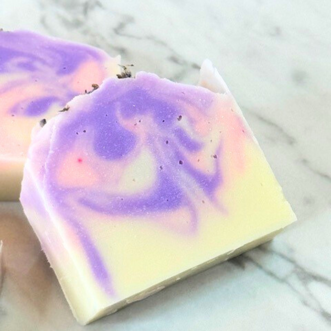 A white soap bar with a pink and purple swirl in the center, topped with natural lavender buds.