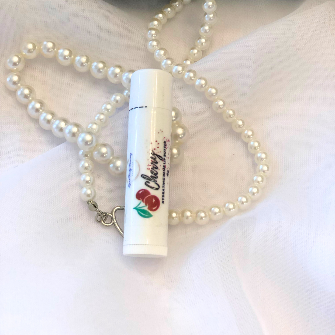 A white lip balm stick with a cherry image on the label, set against a white and pearl background.