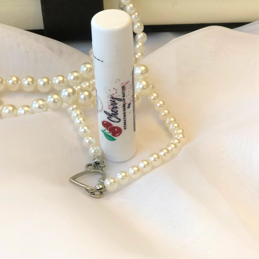 A white lip balm stick with a cherry image on the label, set against a white and pearl background.