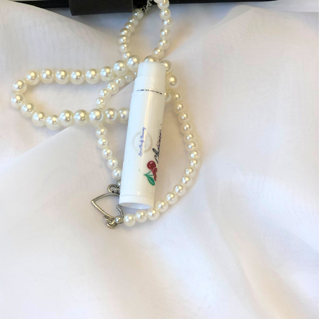 A white lip balm stick with a cherry image on the label, set against a white and pearl background.