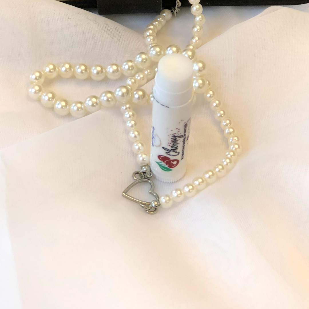 A white lip balm stick with a cherry image on the label, set against a white and pearl background.