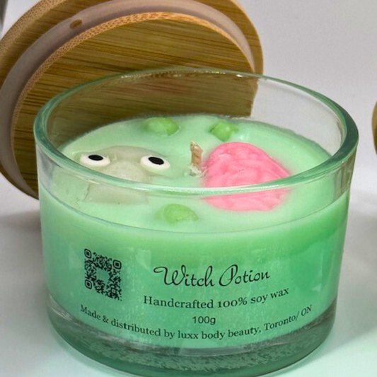 A light green, single-wick candle in a clear jar with a bamboo lid, featuring a skull, pink brain, and bubbles decoration on top—perfect for Halloween.