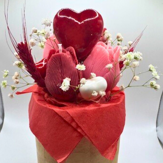 A wooden vase filled with candles shaped like pink and red roses. decorated with big red heart in the middle and botanical flora with many other small hearts