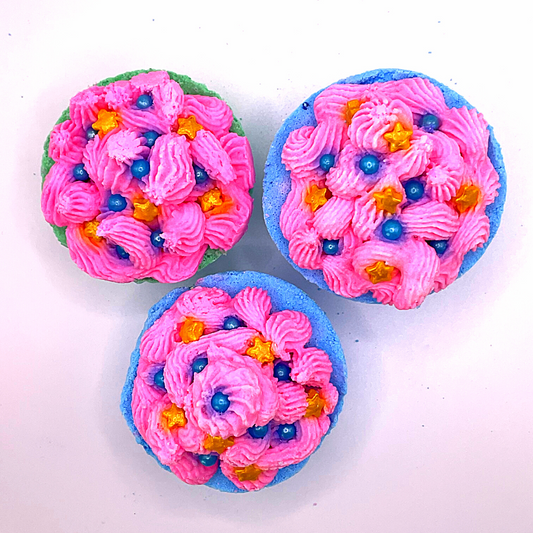 A blue cupcake-shaped bath bomb topped with pink bubble bath icing, topped with blue pearls and golden stars.