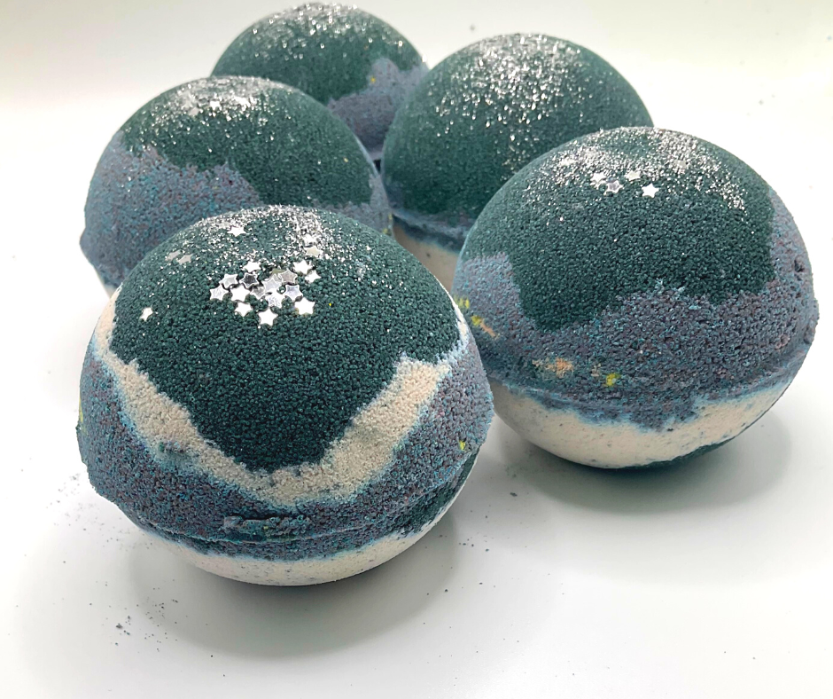 A round bath bomb with black, grey, and white colors, topped with silver stars.