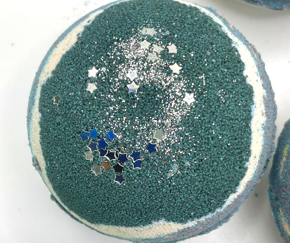 A round bath bomb with black, grey, and white colors, topped with silver stars.
