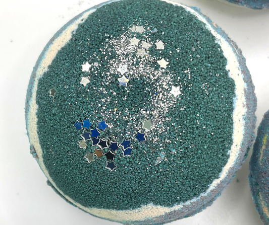A round bath bomb with black, grey, and white colors, topped with silver stars.
