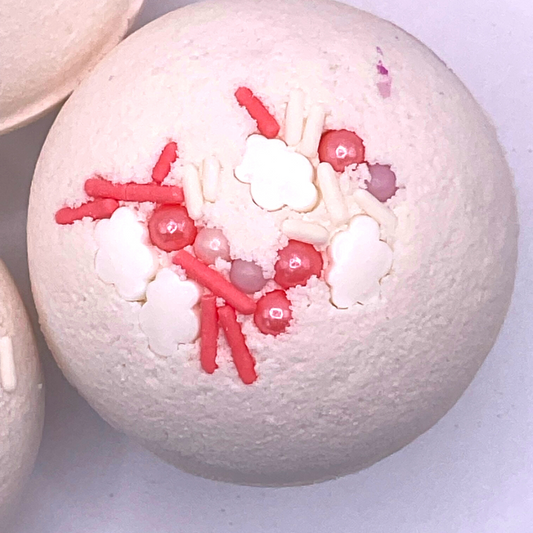 A white round bath bomb topped with pink and purple pearls.