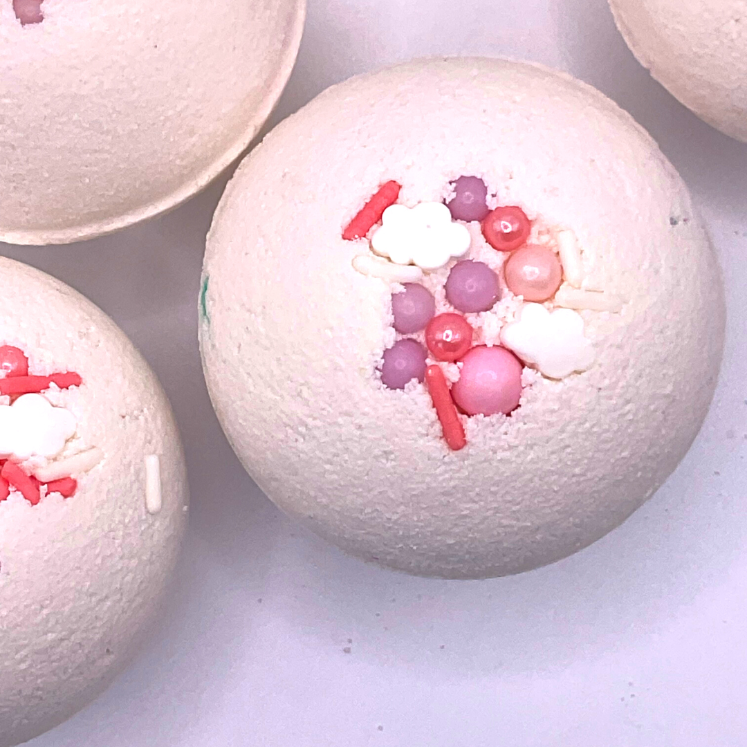 A white round bath bomb topped with pink and purple pearls.