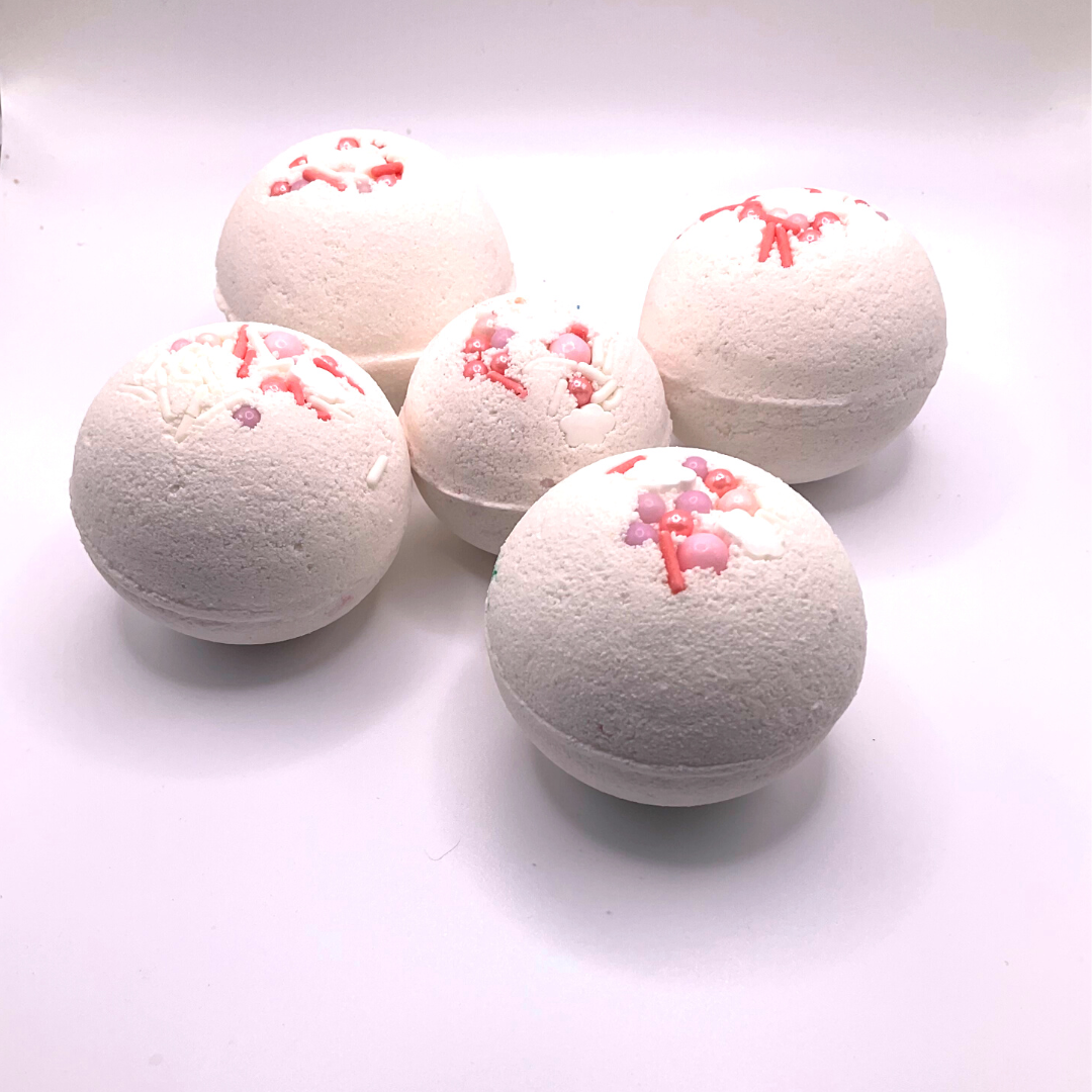 A white round bath bomb topped with pink and purple pearls.