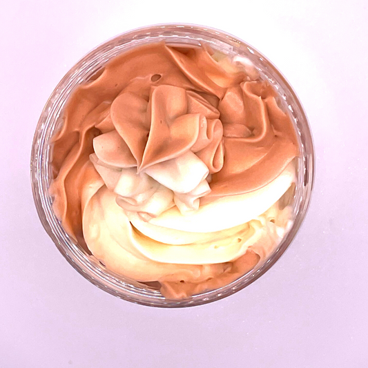 A  top view of a whipped foamy sugar scrub of light brown and off-white colors piped in a clear jar.