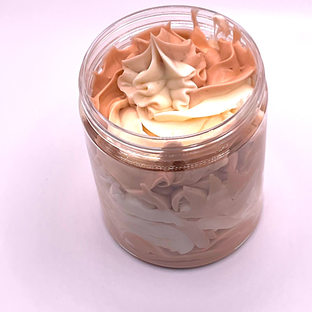 A whipped foamy sugar scrub of light brown and off-white colors piped in a clear jar.