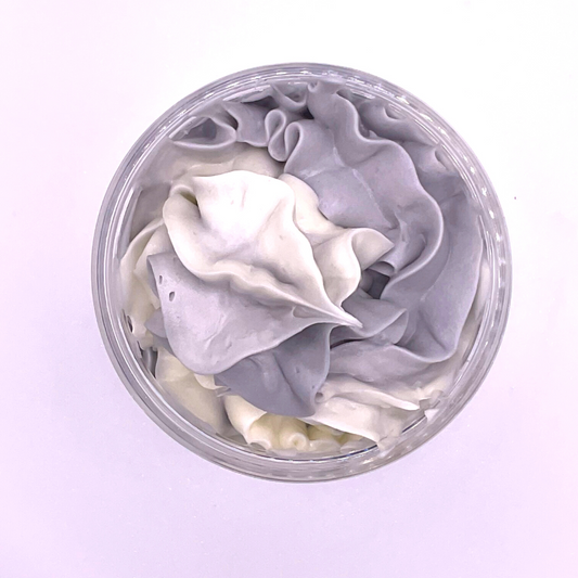 A top view of a whipped foamy sugar scrub of grey and white colors piped in a clear jar.