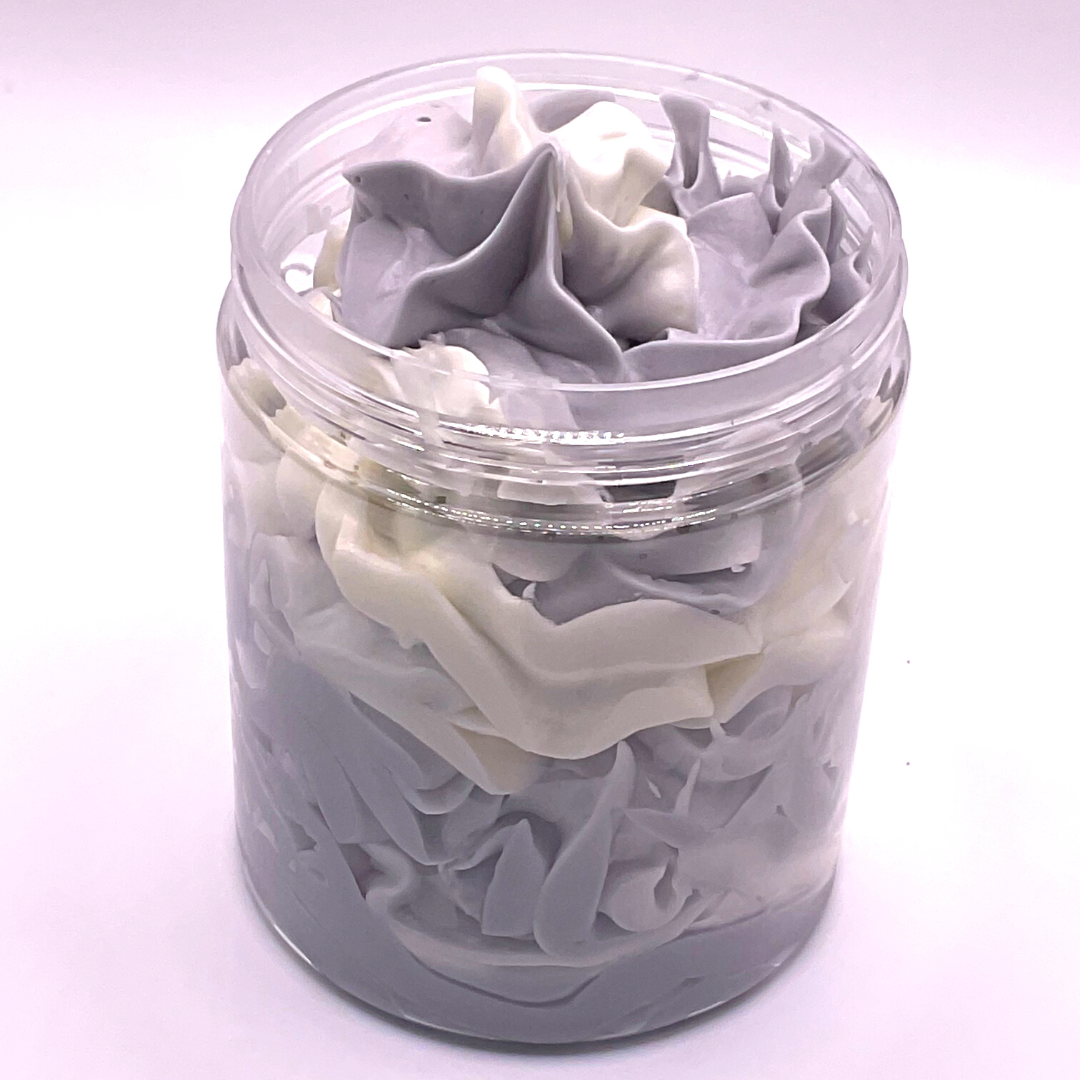 A whipped foamy sugar scrub of grey and white colors piped in a clear jar.