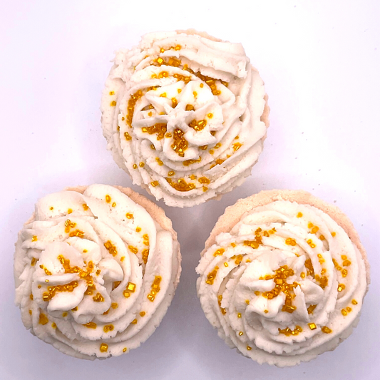 A white cupcake-shaped bath bomb topped with white bubble bath icing, topped with golden pearls.