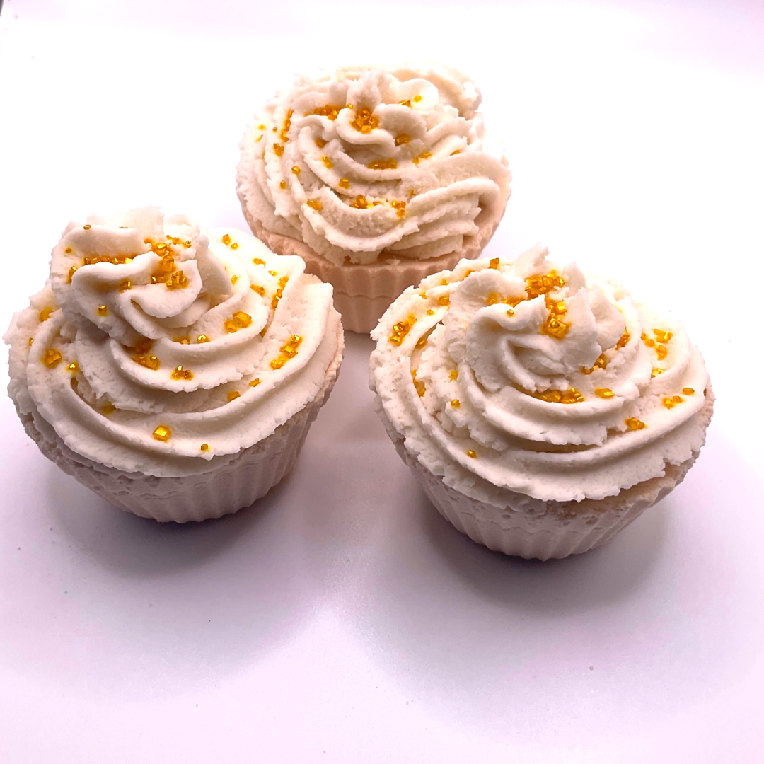 A white cupcake-shaped bath bomb topped with white bubble bath icing, topped with golden pearls.