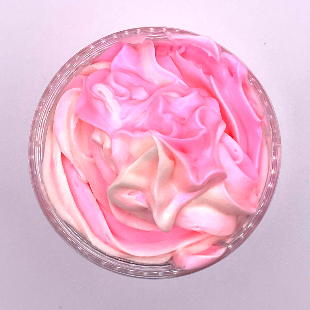 A top view of a whipped foamy sugar scrub of pink and white colors piped in a clear jar.
