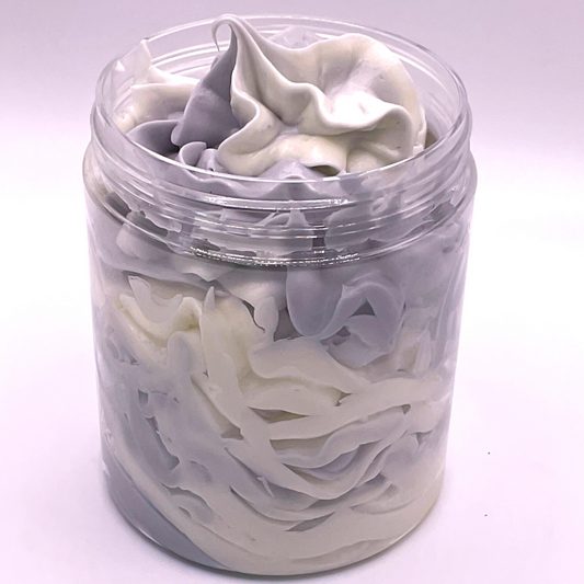 A whipped foamy sugar scrub of grey and white colors piped in a clear jar.