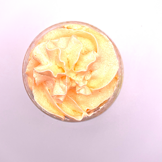 A top view of a whipped foamy sugar scrub of yellow and orange colors piped in a clear jar.