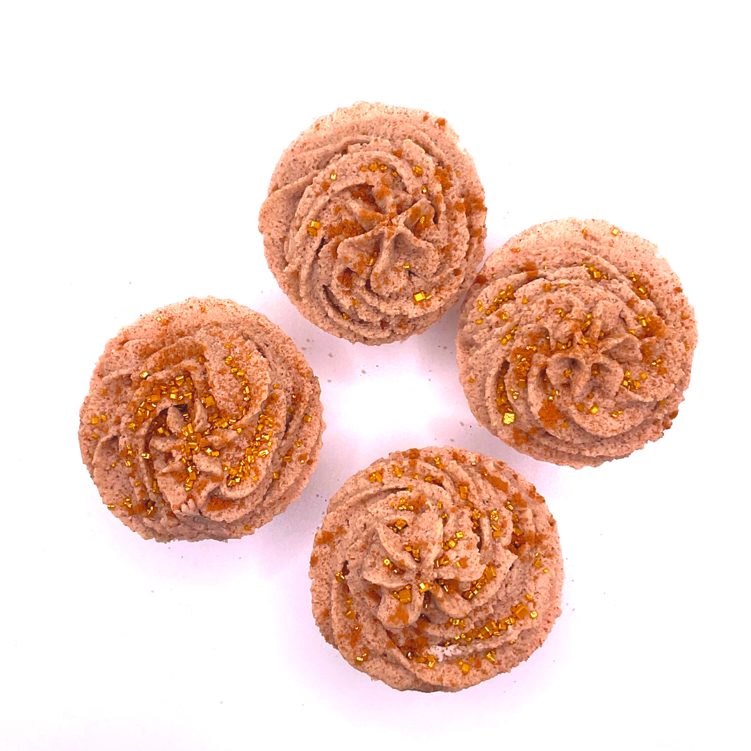 A light brown cupcake-shaped bath bomb topped with light brown bubble bath icing, topped with golden pearls.