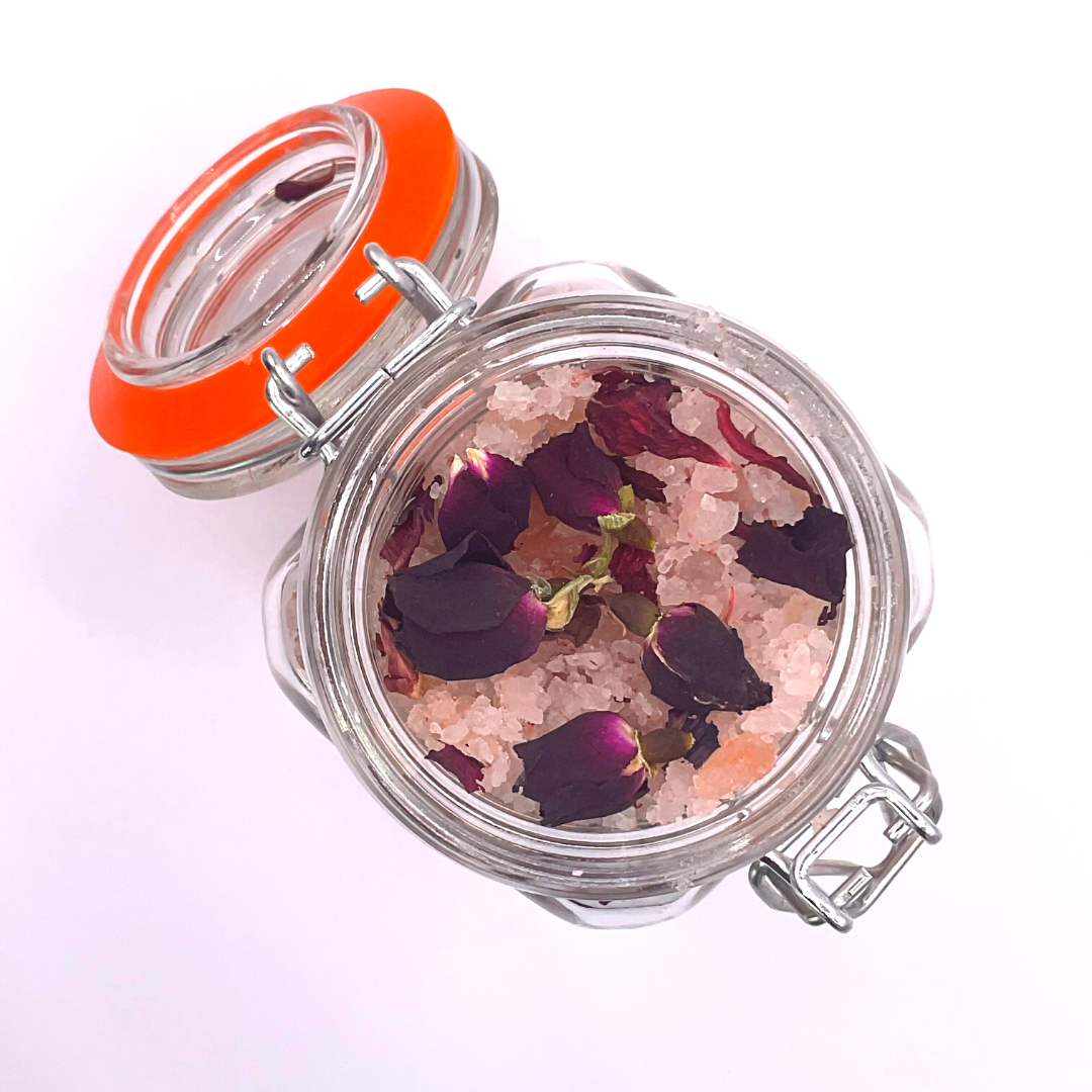 The top view of a clear jar filled with pink Himalayan salts mixed with dried florals and rose buds.
