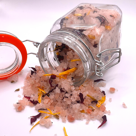 A flipped-over clear jar spilling pink Himalayan salts mixed with dried florals.