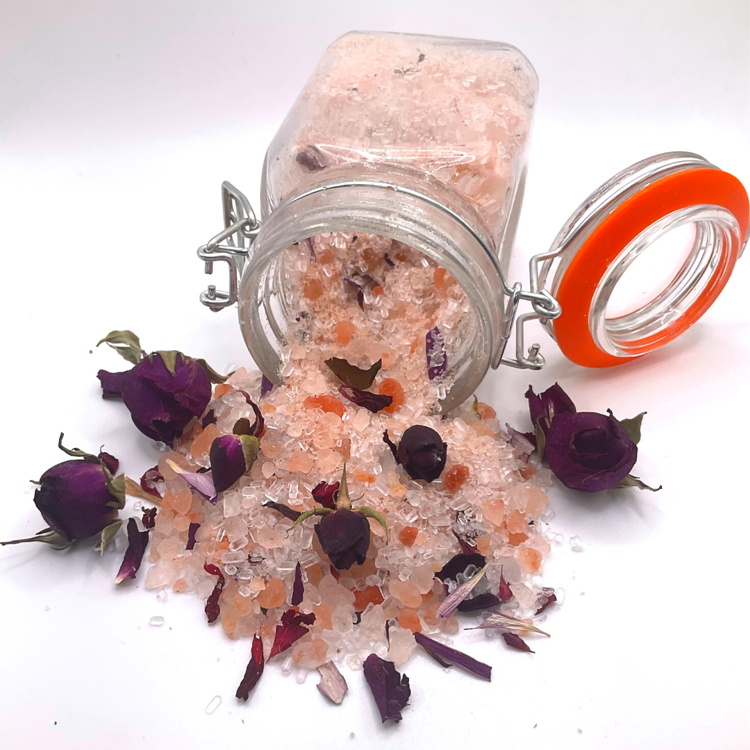 A flipped-over clear jar spilling pink Himalayan salts mixed with dried florals and rose buds.