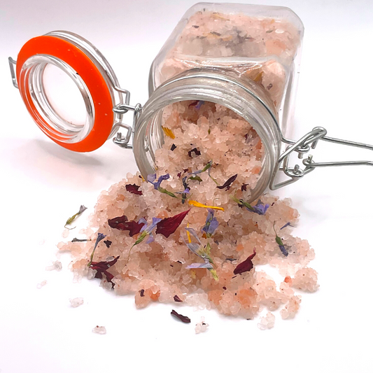 A flipped-over clear jar spilling pink Himalayan salts mixed with dried florals.