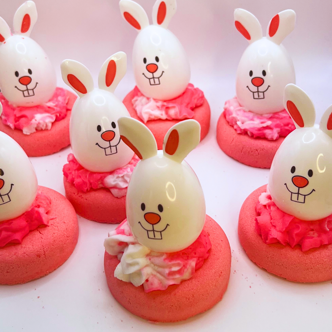 A pink donut-shaped bath bomb topped with pink and white bubble bath icing and a bunny-shaped egg decoration.