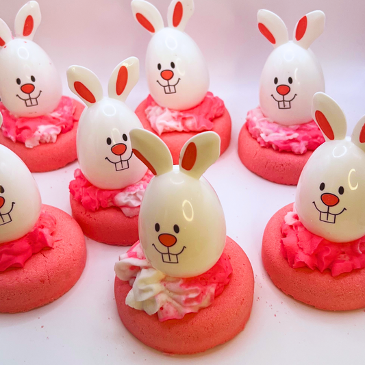 A pink donut-shaped bath bomb topped with pink and white bubble bath icing and a bunny-shaped egg decoration.